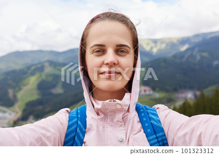 Shot of pretty young female tourist makes selfie in mountain. Woman traveler having active recreation in mountains. Travel, tifestyle, adventure, active vacations, outdoor photographing concept. Shot of pretty young female tourist makes selfie in mountain. Woman traveler having active recreation in mountains. Travel, tifestyle, adventure, active vacations, outdoor photographing concept. 101323312