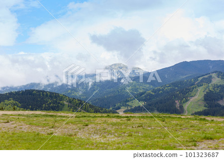 View of mountain with rocky foreground, green meadows, tourist path in distance, beautiful nature, amazing landscape, briliant scenery, green field on the bottom of mountains, blue sky with clouds. 101323687