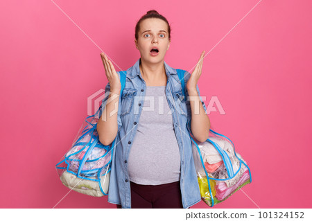 European woman with raising palms and widely opened mouth, being shocked, surprised, expectant mother with big belly, holds stuff in bags, isolated on pink background, wearing denim, jacket. 101324152
