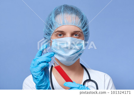 Close up portrait of hard working nurse wearing medical hat, mask and gloves, holding test tube with blood for covid 2019, waiting for results, having dangerous work. People and epidemic concept. 101324171