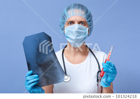 Positive coronavirus test and doctor comparing it to lung X-ray, having scared and worried facial expression, wearing protective mask, gloves, disposable hat. Covid 19, pandemic, qaurantine concept. Positive coronavirus test and doctor comparing it to lung X-ray, having scared and worried facial expression, wearing protective mask, gloves, disposable hat. Covid 19, pandemic, qaurantine concept. 101324218