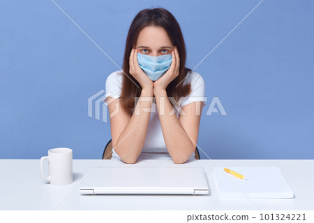 Coronavirus, quarantine concept. Online training education and freelance work. Attractive lady wearing protective mask sitting in front of closed laptop, girl studing remotely, student looks tired. Coronavirus, quarantine concept. Online training education and freelance work. Attractive lady wearing protective mask sitting in front of closed laptop, girl studing remotely, student looks tired. 101324221