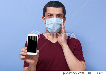 Picture of emotional shocked guy putting one hand close to face, holding his smartphone, being in panic, using device, staying at home, being scared by coronavirus. People and pandemic concept. 101324375