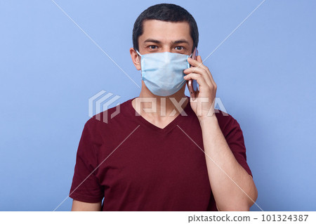 Indoor photo of happy handsome man having conversation over phone, looking directly at camera, putting smartphone to ear, getting good news, being in antibacterial mask. People and covid19 concept. Indoor photo of happy handsome man having conversation over phone, looking directly at camera, putting smartphone to ear, getting good news, being in antibacterial mask. People and covid19 concept. 101324387