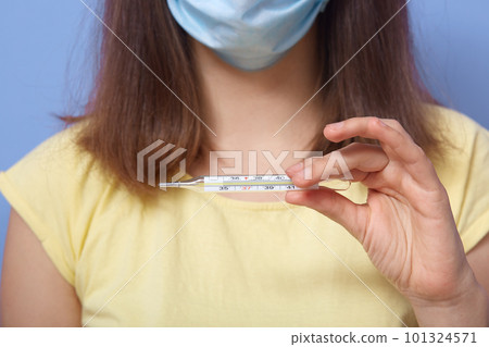 Close up picture of unknown short haired model in antibacterial mask, wearing t shirt, holding thermometer, being in quaratine, showing result, checking symptoms. People and disease concept. 101324571