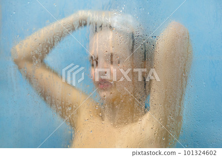 Photo of female with naked perfect body takes shower against dewy glass in bathroom, washes in shower cabine, feels relax and rejuvenation, has pure healthy soft skin. Body care concept 101324602