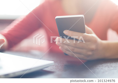 Cropped shot of female hand holding her smartphone in hand reading message via email or making call sitting at wooden table and working with her laptop. Film effect. Technology concept. Cropped shot of female hand holding her smartphone in hand reading message via email or making call sitting at wooden table and working with her laptop. Film effect. Technology concept. 101324976