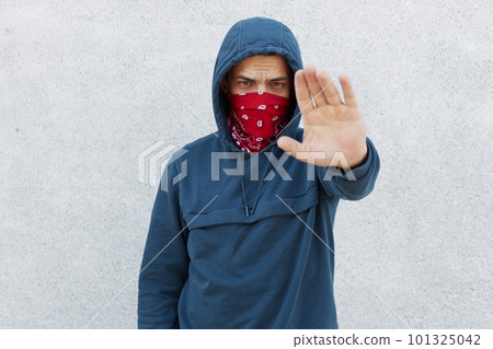 Portrait of serious disappointed protester against black citizens lawlessness,guy showing stop gesture with his palm, stop murder people, activist wearing jumper with hoody and bandana mask. Portrait of serious disappointed protester against black citizens lawlessness,guy showing stop gesture with his palm, stop murder people, activist wearing jumper with hoody and bandana mask. 101325042