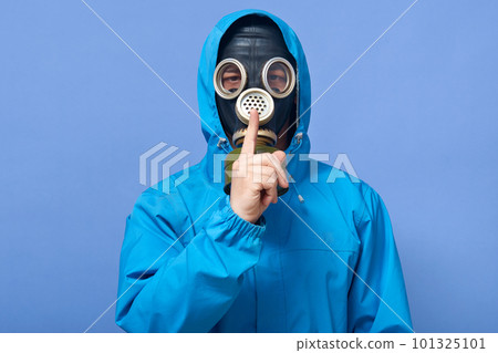 Studio shot of scientist wearing uniform and gas mask, posing isolated over blue background, keeping finger near lips, calls on keep silence, ecologist explores air pollution level. Ecology concept. 101325101