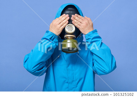 Horizontal image of man in protection suit with gas mask on face covering eyes, being under threat, standing isolated over blue background in studio, staying alone. People and disaster concept. Horizontal image of man in protection suit with gas mask on face covering eyes, being under threat, standing isolated over blue background in studio, staying alone. People and disaster concept. 101325102