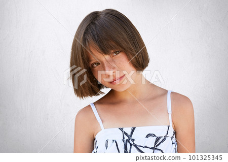 Pretty little girl with freckles, dark eyes and short hairstyle wearing summer white dress posing against white background having confident and serious look. Children, lifestyle, beauty concept Pretty little girl with freckles, dark eyes and short hairstyle wearing summer white dress posing against white background having confident and serious look. Children, lifestyle, beauty concept 101325345