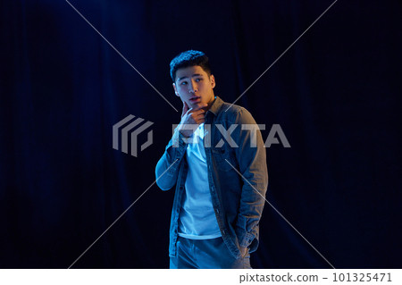 Charismatic young man in casual stylish clothes posing against dark background in neon light. Concept of human emotions and lifestyle Charismatic young man in casual stylish clothes posing against dark background in neon light. Concept of human emotions and lifestyle 101325471
