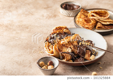 Crepes with chocolate and hazelnuts on beige background. Thin pancakes as delisious breakfast or dessert concept, Pancake day, Maslenitsa. Copy space 101325664