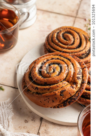 Twisted buns with poppy seeds for morning breakfast tea on beige tile background close up. Swirl brioche with poppy seeds Twisted buns with poppy seeds for morning breakfast tea on beige tile background close up. Swirl brioche with poppy seeds 101325694
