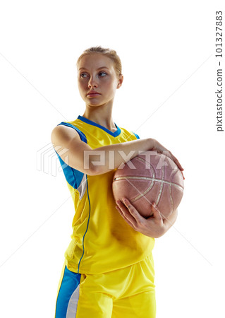 Portrait of young girl, female basketball player in yellow uniform posing with ball against white studio background. Concept of professional sport 101327883
