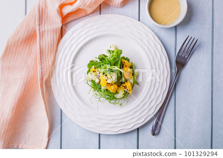 Salad with microgreens of peas, spinach, celery, orange, sesame seeds and dressing in plate on white wooden background. 101329294
