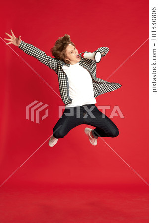One young guy, student wearing casual style clothes jumping and screaming through megaphone over red studio background with pleasure. Breaking news One young guy, student wearing casual style clothes jumping and screaming through megaphone over red studio background with pleasure. Breaking news 101330806