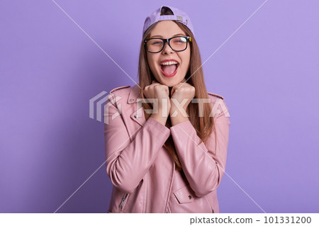 Indoor portrait of charismatic emotional female expressing her feelings, keeping fists close to face, opening mouth widely, wearing accessories, being in high spirits. Youth and emotions concept. Indoor portrait of charismatic emotional female expressing her feelings, keeping fists close to face, opening mouth widely, wearing accessories, being in high spirits. Youth and emotions concept. 101331200