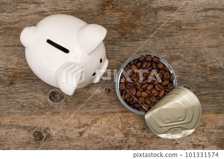 Piggy bank next to opened tin-can full of roasted coffee beans Piggy bank next to opened tin-can full of roasted coffee beans 101331574