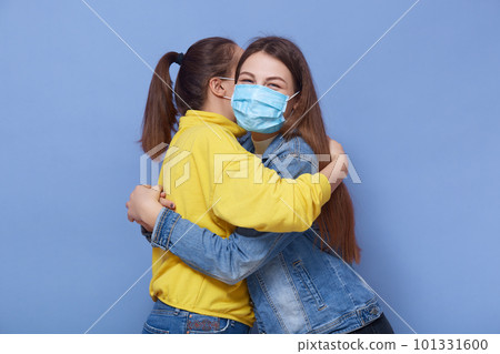 Studio shot of two young happy friends meeting each other during quarantine, wearing antibacterial masks, close contact, not sticking to rules, wearing casual clothes. People and health concept. 101331600