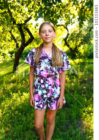 Summer teen girl. Defocus beautiful smiling teenage girl in dress standing against green summer background. High girl 12 or 13 years old on summer lawn. Vertical. Out of focus 101331665