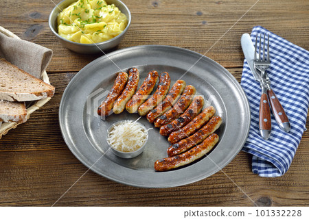 Ten fried Nuremberg sausages with horseradish served on a pewter plate with a bowl of potato salad  101332228
