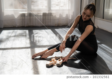 An Asian ballerina sits on the floor and puts on pointe shoes. An Asian ballerina sits on the floor and puts on pointe shoes. 101332561
