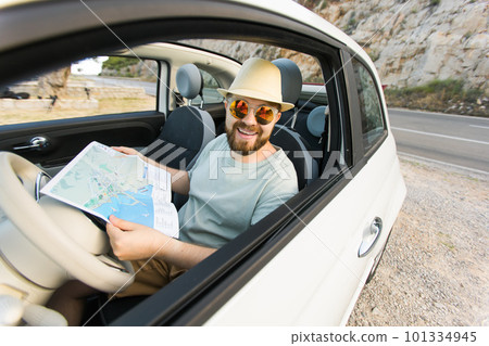 Hipster man looking on location navigation map in car, tourist traveler driving and hold in male hands europe cartography, view and plan tourist way road, trip in transportation cabriolet auto 101334945