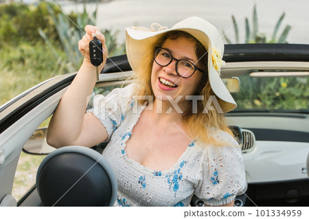 Car driver woman smiling showing new car keys and car. Female driving rented cabrio on summer vacation Car driver woman smiling showing new car keys and car. Female driving rented cabrio on summer vacation 101334959