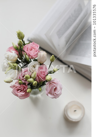 Home decoration and interior. Beautiful burning candle with flowers and book on white table. Details of still life in the home interior of living room. Cozy spring concept. 101335576