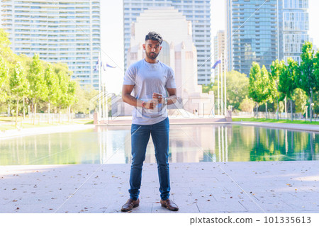 An Indian man standing in front of the water surface in a bright green park 101335613