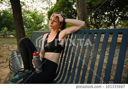 Tired athlete female runner in sportswear sitting on a park bench resting after morning workout Tired athlete female runner in sportswear sitting on a park bench resting after morning workout 101335687