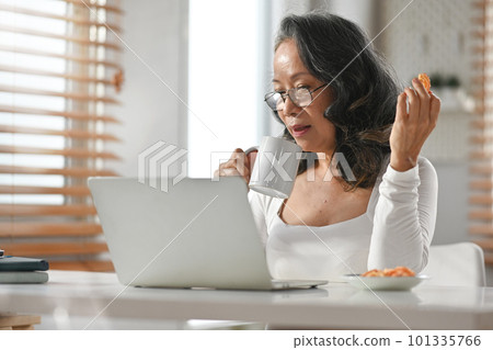 Portrait of beautiful middle aged woman drinking hot coffee and looking at laptop screen 101335766