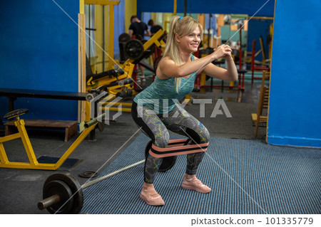 Woman performs squats with exercise rubber band wrapped around calves Woman performs squats with exercise rubber band wrapped around calves 101335779