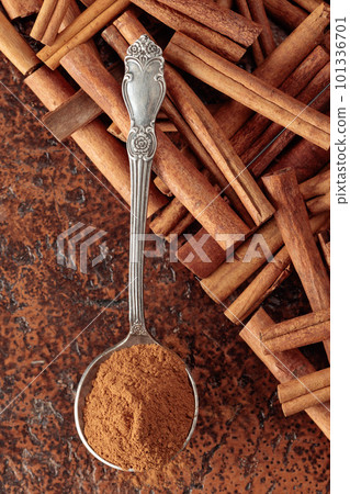 Cinnamon powder in a spoon and cinnamon sticks on a brown background. 101336701