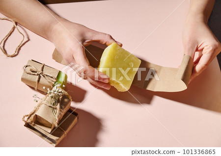 The concept of spa and natural cosmetics with essential oils for skin and body care. Female hands wrapping bars of natural soap for sale in local markets. Purity. Hygiene. Skin and body care concept 101336865
