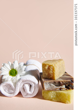 Spa set with two rolled white towels, chamomile flower and stack of organic natural soap bars with natural ingredients on isolated beige background. Vertical photo. Still life. Copy advertising space Spa set with two rolled white towels, chamomile flower and stack of organic natural soap bars with natural ingredients on isolated beige background. Vertical photo. Still life. Copy advertising space 101337371