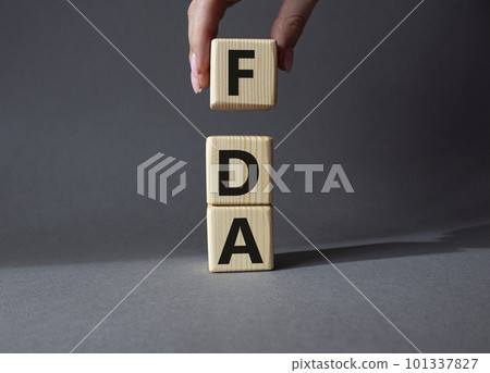 FDA - Food Drug Administration symbol. Wooden cubes with word FDA. Doctor hand. Beautiful grey background. Medical and Food Drug Administration concept. Copy space. FDA - Food Drug Administration symbol. Wooden cubes with word FDA. Doctor hand. Beautiful grey background. Medical and Food Drug Administration concept. Copy space. 101337827
