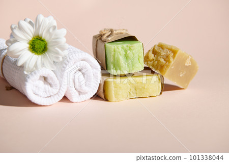 Spa set with two rolled white towels, chamomile flower and stack of organic natural soap bars with natural ingredients on isolated beige background. Horizontal shot. Still life. Copy advertising space 101338044