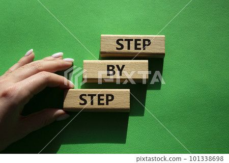 Step by step symbol. Wooden blocks with words Step by step. Beautiful green background. Businessman hand. Business concept. Copy space. Step by step symbol. Wooden blocks with words Step by step. Beautiful green background. Businessman hand. Business concept. Copy space. 101338698