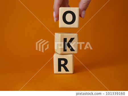 OKR objectives and key results symbol. Wooden cubes with words OKR objectives and key results. Businessman hand. Beautiful orange background. Business and OKR concept. Copy space. 101339160