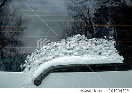 windshield wiper of the rear window of a car covered with a layer of snow thawed from the glass as a result of heating with heating strips, close-up. windshield wiper of the rear window of a car covered with a layer of snow thawed from the glass as a result of heating with heating strips, close-up. 101339759
