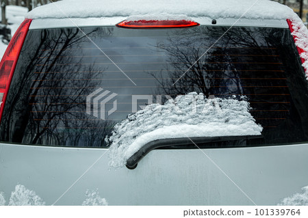 rear window of car with windshield wiper covered with snow and blocked, gray vehicle with red brake lights, nobody. 101339764