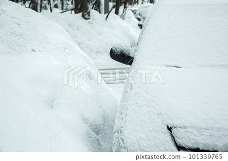huge drifts of snow on the street with parked snow-covered cars, a featureless vehicle frostbitten by winter weather. 101339765