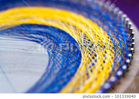 Colored thread mandala on a wooden board with nails. Mandala Moon Harmony Sun esotericism and psychology pictures from yellow and blue silk threads. 101339840