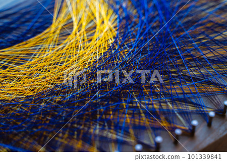 Colored thread mandala on a wooden board with nails. Mandala Moon Harmony Sun esotericism and psychology pictures from yellow and blue silk threads. 101339841