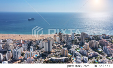 Aerial view of Portuguese city of Portimao with high-rise buildings on the coast with beaches. Tourist cruise liner in background in sea. Aerial view of Portuguese city of Portimao with high-rise buildings on the coast with beaches. Tourist cruise liner in background in sea. 101341535
