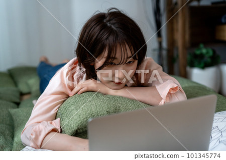 Young woman lying down and using a laptop Young woman lying down and using a laptop 101345774