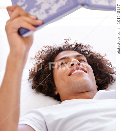 Lazy morning reading. Close-up shot of a handsome young man lying down on his back and holding a book. Lazy morning reading. Close-up shot of a handsome young man lying down on his back and holding a book. 101348127