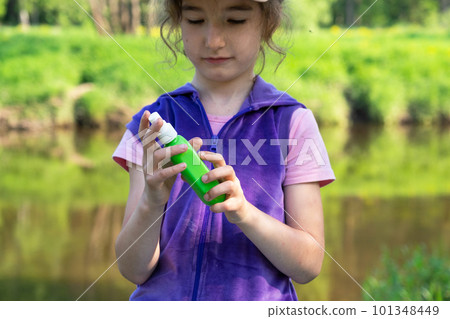 Girl sprays mosquito spray on the skin in nature that bite her hands and feet. Protection from insect bites, repellent safe for children. Outdoor recreation, against allergies. Summer time 101348449